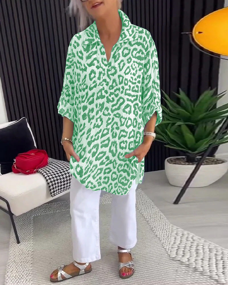 Green leopard print blouse with collar, worn over white pants, in a chic indoor setting with plants and modern decor.