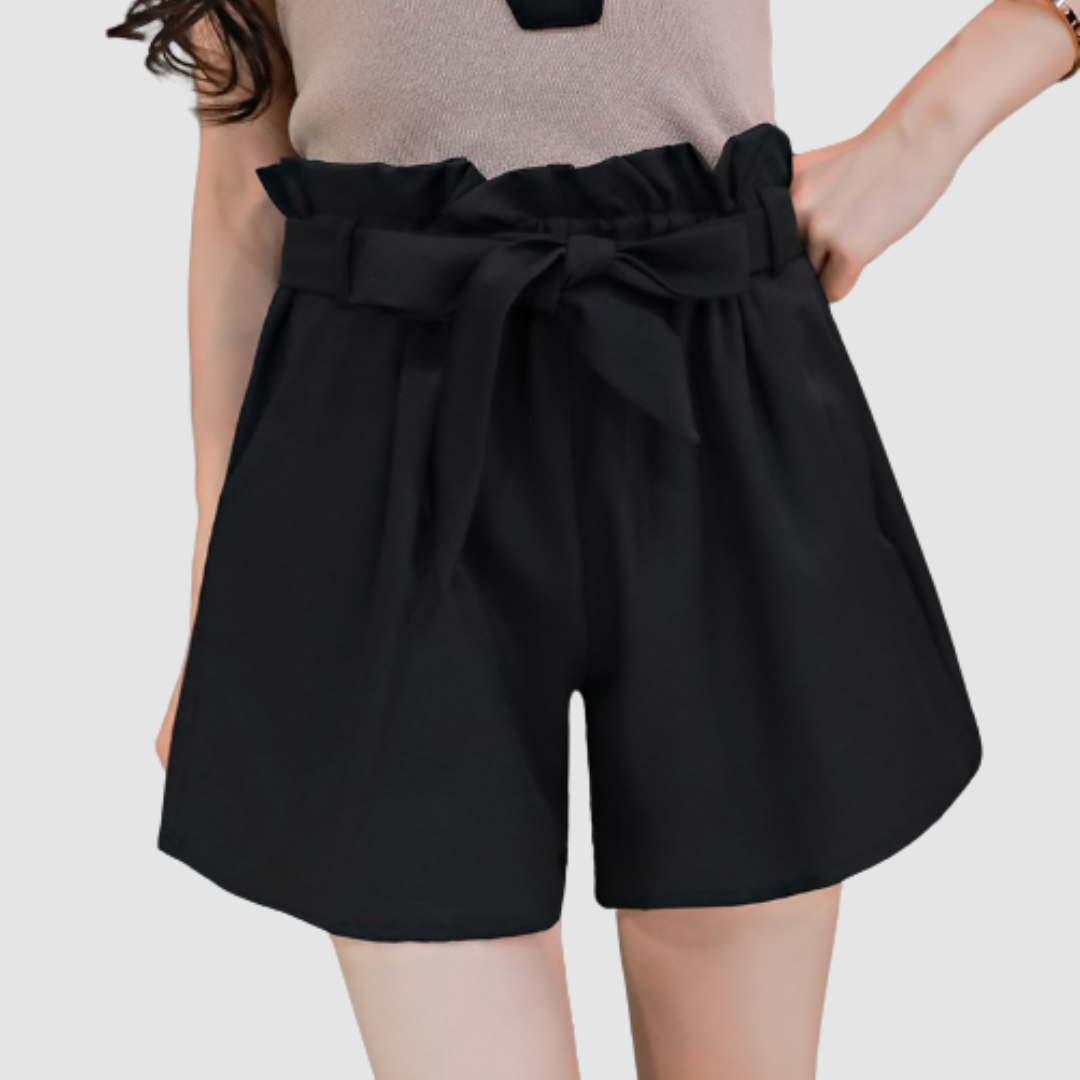 Black paperbag waist shorts with a bow, paired with a beige top in a studio background.