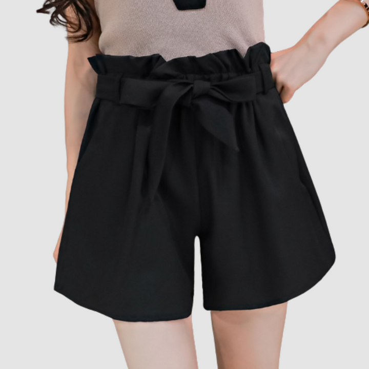 Black paperbag waist shorts with a bow, paired with a beige top in a studio background.