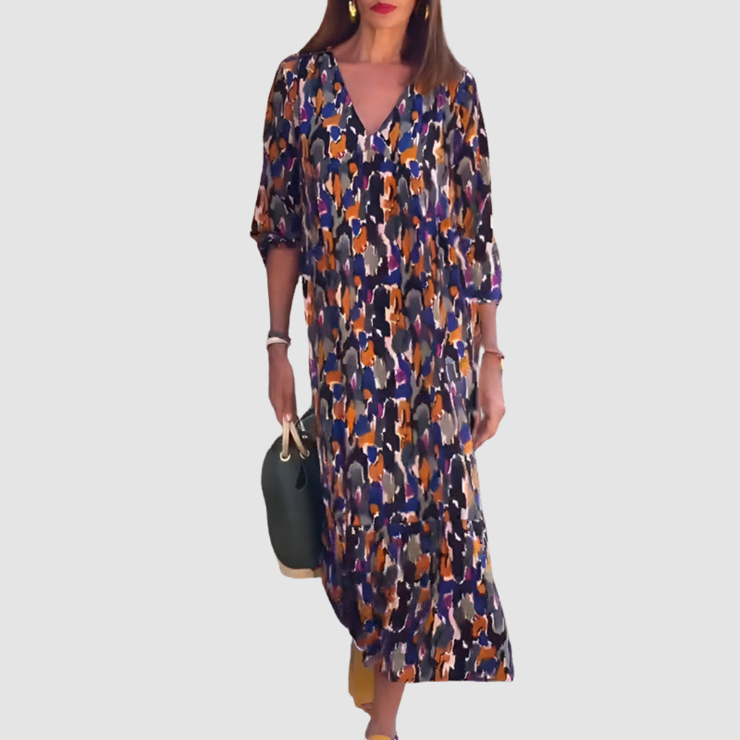 A woman in an abstract multicolor V-neck dress, holding a green handbag, set against a plain backdrop.