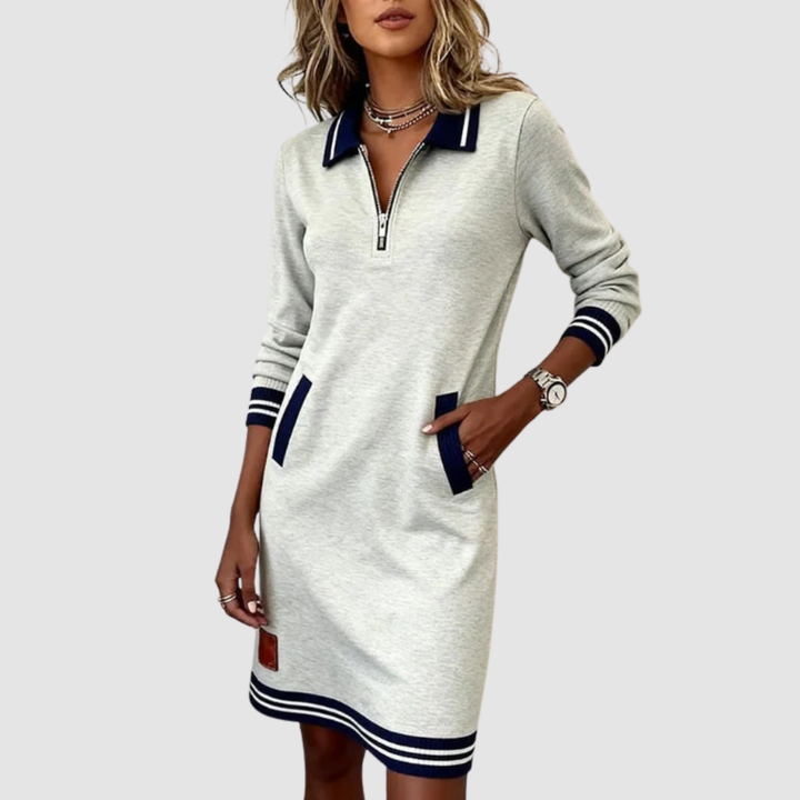 Casual light gray zip-neck dress with navy accents and pockets, worn by a woman with accessories in a studio setting.