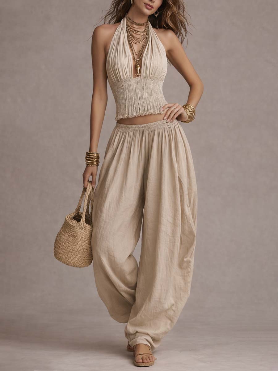 Beige two-piece set with a textured top and flowing pants, accessorized with gold bangles and a basket bag. Studio background.