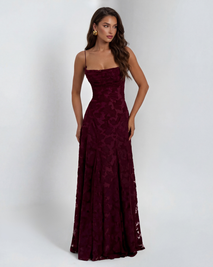 Model wearing a burgundy maxi dress with floral pattern and thin straps, studio setting.