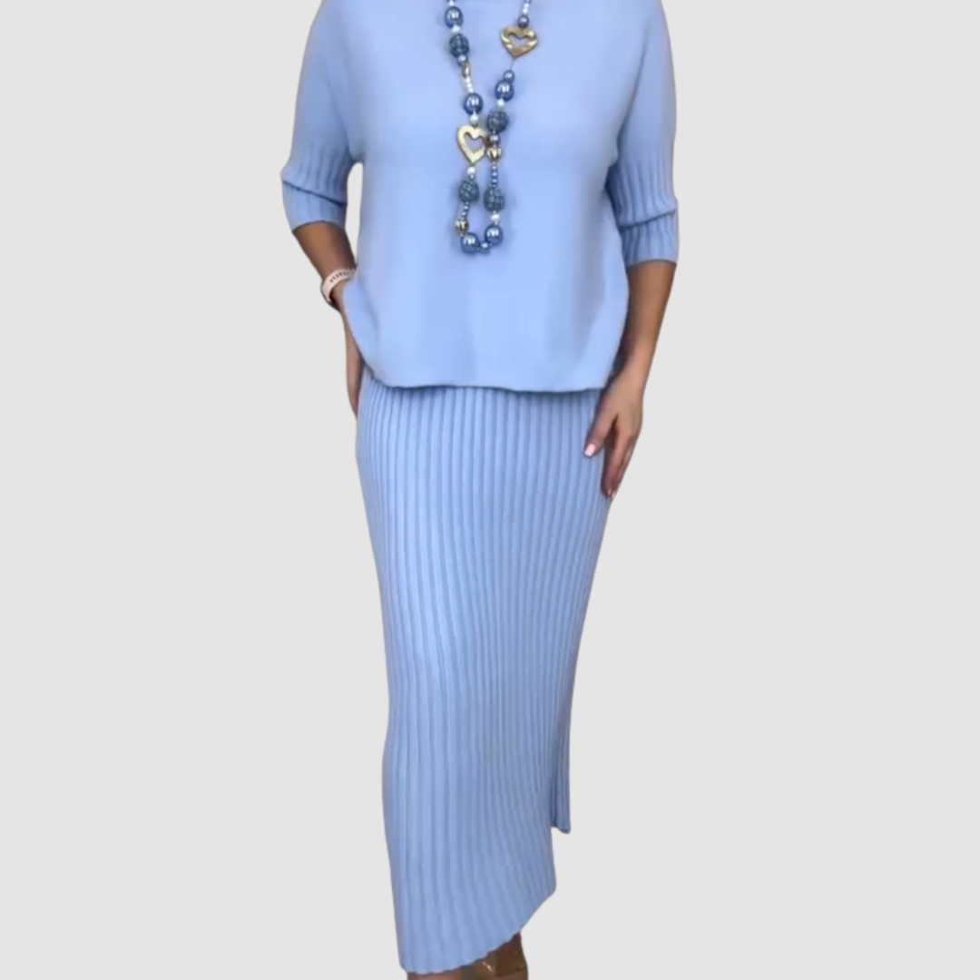 Light blue 2-piece set with ribbed skirt and loose top, worn with a long, heart-themed necklace on plain background.