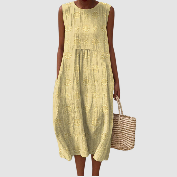 Yellow sleeveless summer dress with floral patterns, model holding a woven basket, white background.