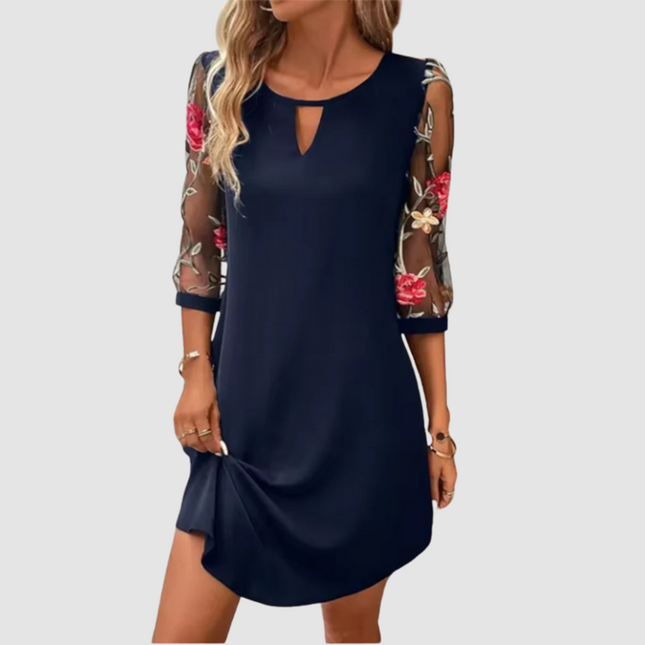 Navy blue summer dress featuring floral print sheer sleeves, modeled indoors against a neutral background.