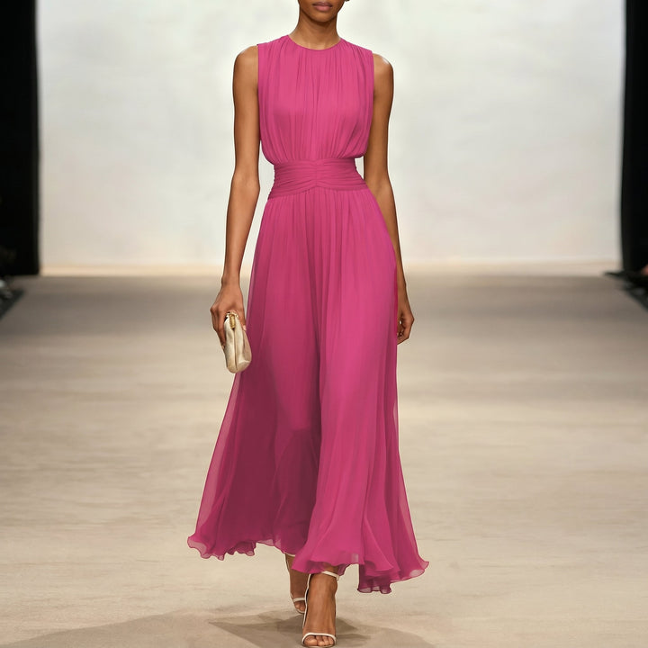 Pink elegant dress with flowing design, model holding a clutch indoors.