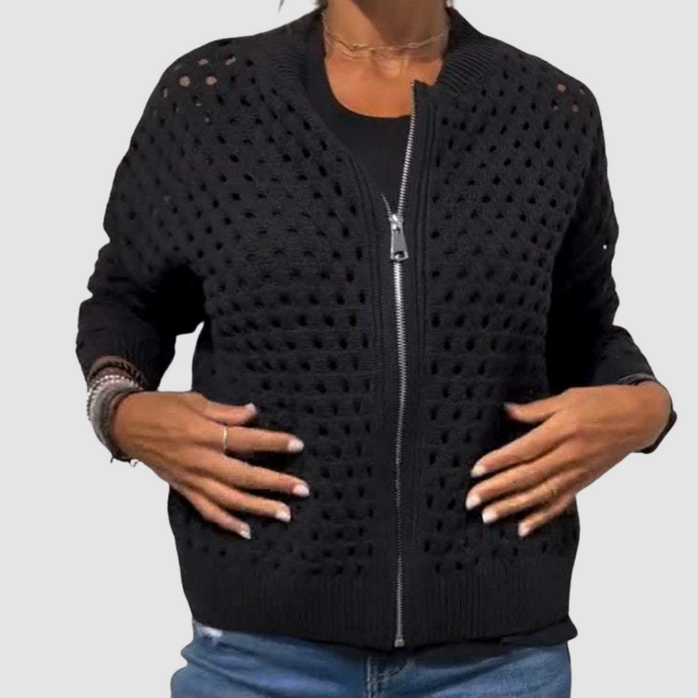 Black knitted cardigan with a zip closure and perforated texture, worn casually with jeans in a studio setting.