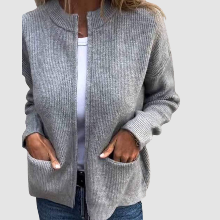 Gray cozy cardigan worn over a white t-shirt with hands in pockets. Neutral background.