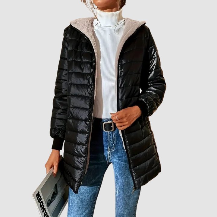 Woman in a black winter coat with a white turtleneck and blue jeans, holding a magazine, studio setting.