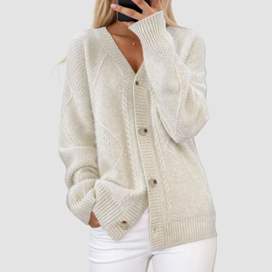 White knitted V-neck cardigan with button accents, worn by person with hand in pocket, set against a light gray background.