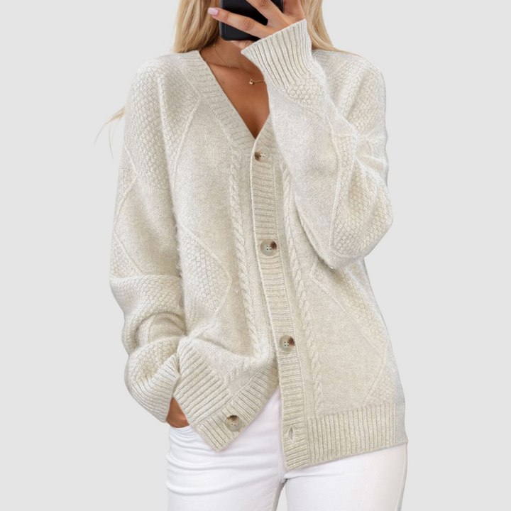 White knitted V-neck cardigan with button accents, worn by person with hand in pocket, set against a light gray background.