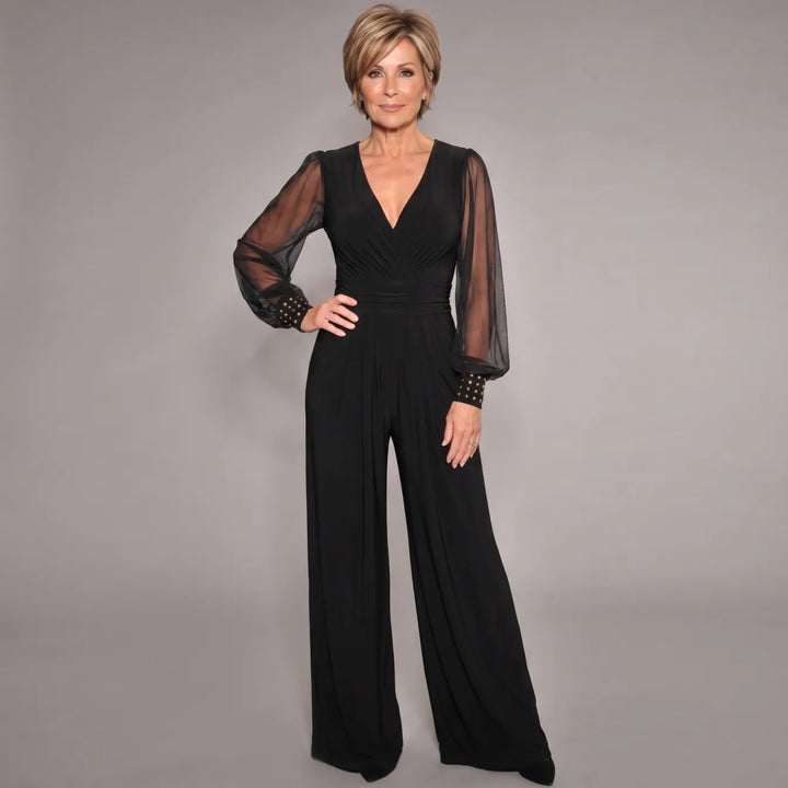 Elegant black jumpsuit with sheer long sleeves and gold accents, modeled in a studio setting.
