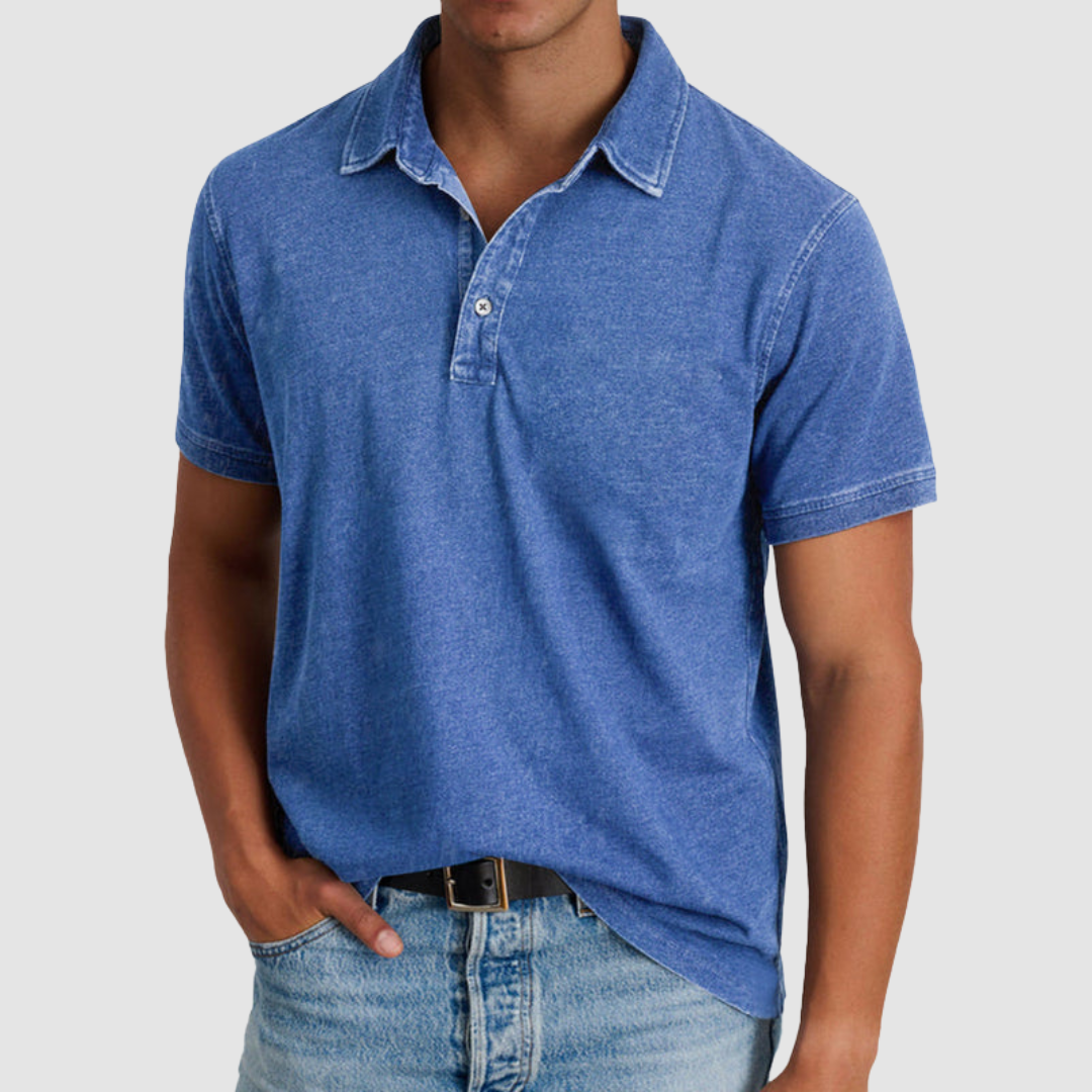 Model wearing a blue classic collared polo with short sleeves and buttoned placket, paired with light jeans in a studio setting.