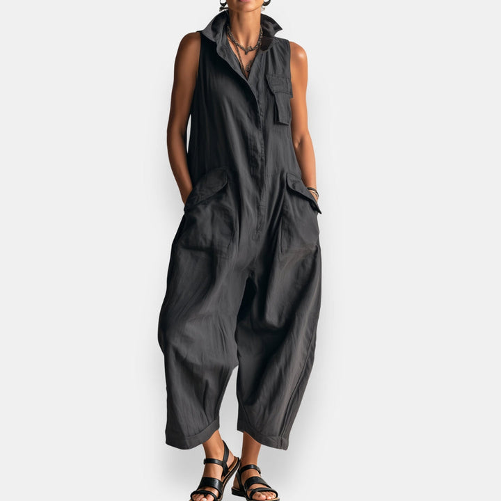 Dark sleeveless cargo jumpsuit with collar and pockets, modeled standing against white background.