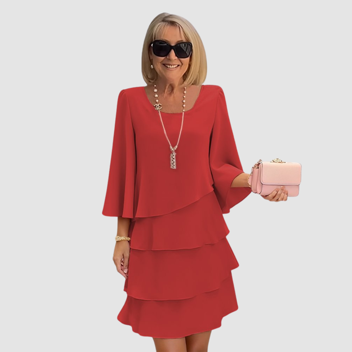 Elegant woman in a red tiered dress with bell sleeves, holding a pink purse, on a light gray background.