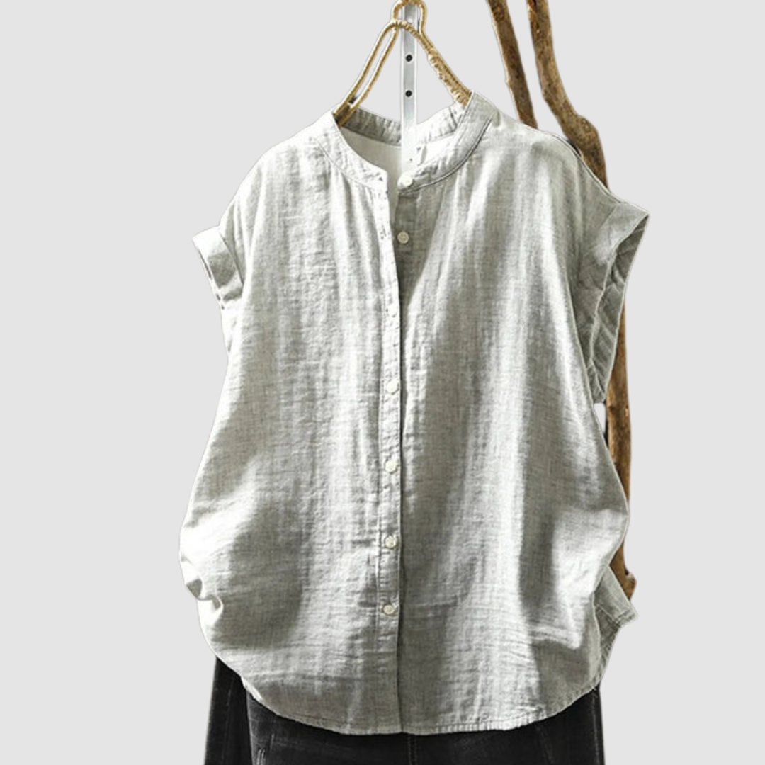 Light gray vintage shirt with a soft texture and short sleeves, hanging on a rustic branch against a gray background.
