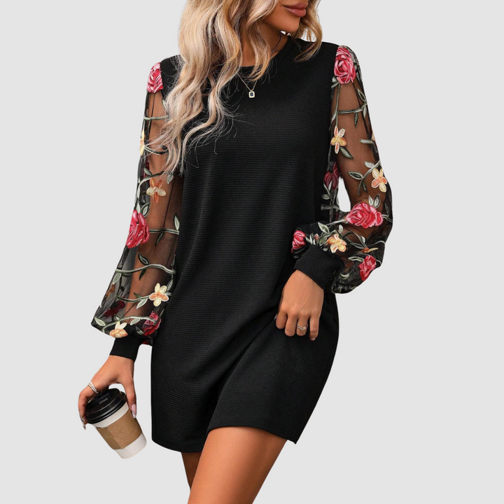Black dress with floral lace sleeves, woman holding a coffee cup. Studio background.