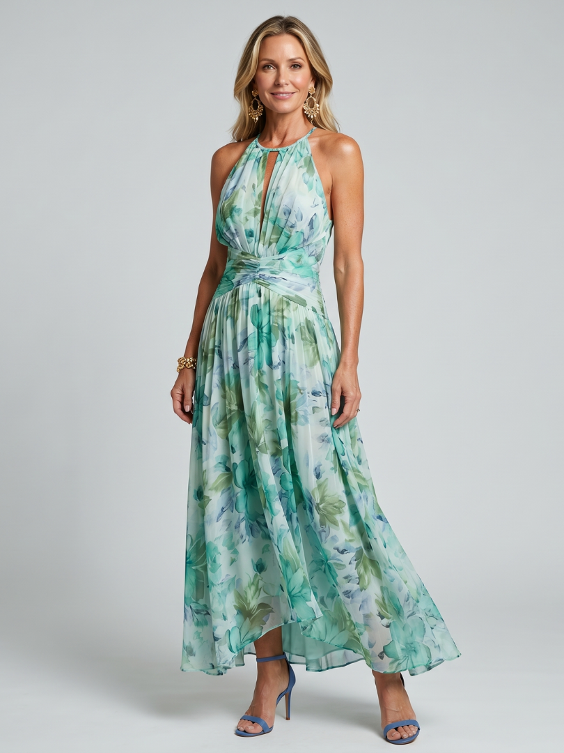 Woman in green floral maxi dress with halter neck and blue heels, posing in studio setting.