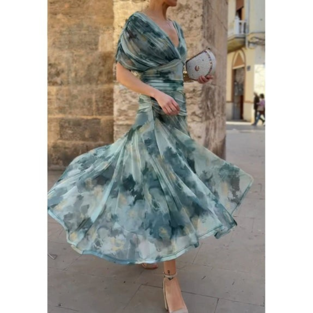 Woman in a green floral corset dress twirling on a street with a stone wall and background buildings.