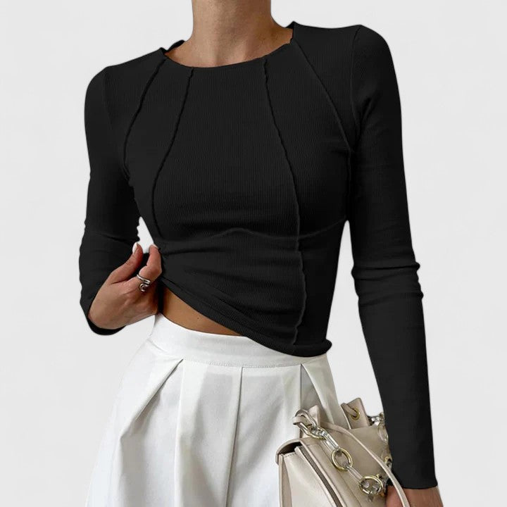 Black long-sleeve top with curved seam details, paired with a white skirt and beige handbag, on a plain white background.