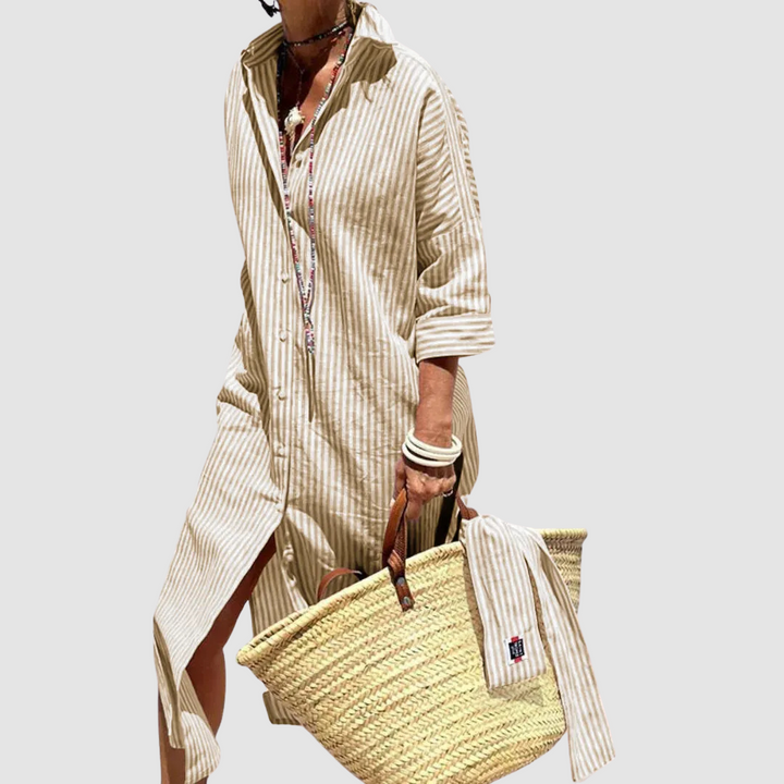 Woman wearing a beige striped button-up summer dress with rolled sleeves, paired with a woven tote, studio background.