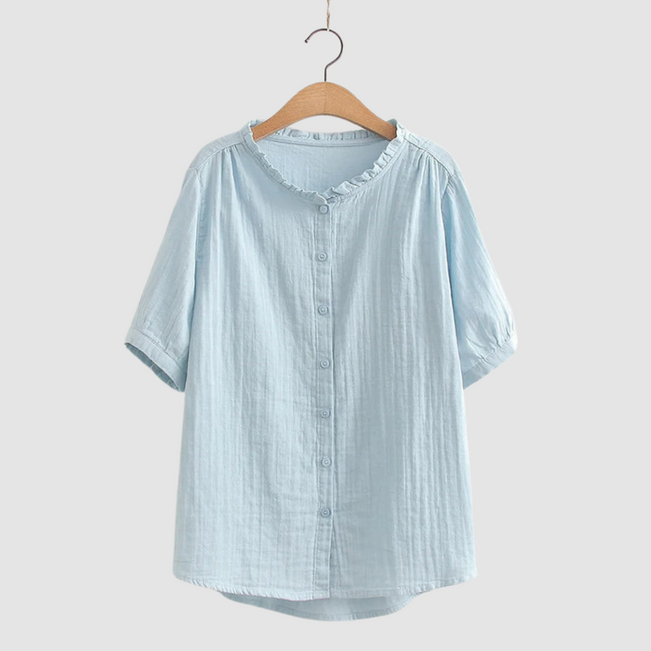 Light blue button-up shirt with ruffled collar on wooden hanger, studio background.