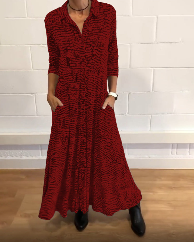 Red-patterned maxi dress with 3/4 sleeves and collar, worn indoors against a white brick wall.