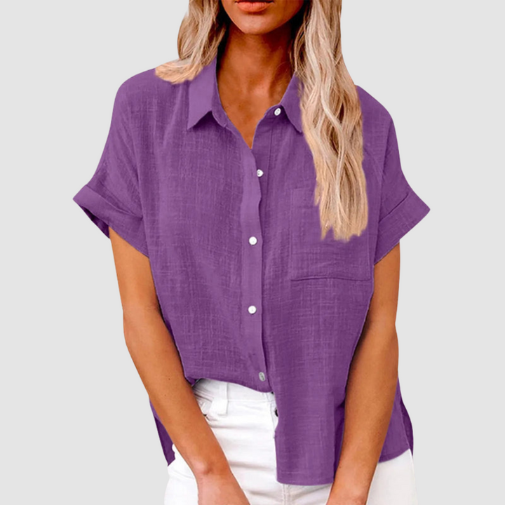 Purple casual blouse with short sleeves and front buttons, worn in white jeans. Studio background.