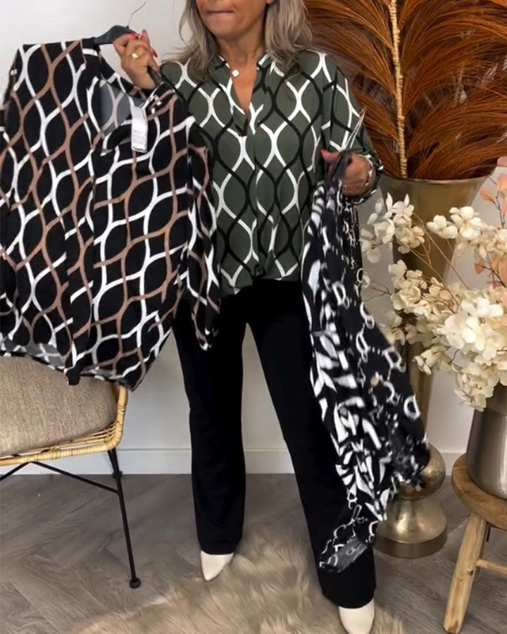 Person holding brown and black graphic print blouses, wearing a green print top, in a cozy room with soft furnishings and plants.