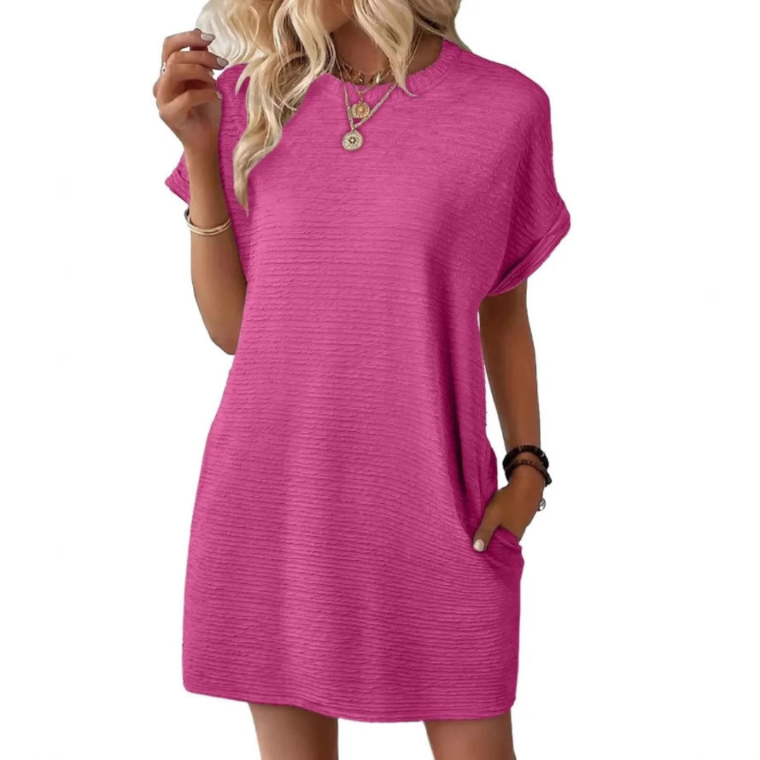 Vibrant pink casual dress with short sleeves and a relaxed fit, worn by a model with necklaces in a studio setting.