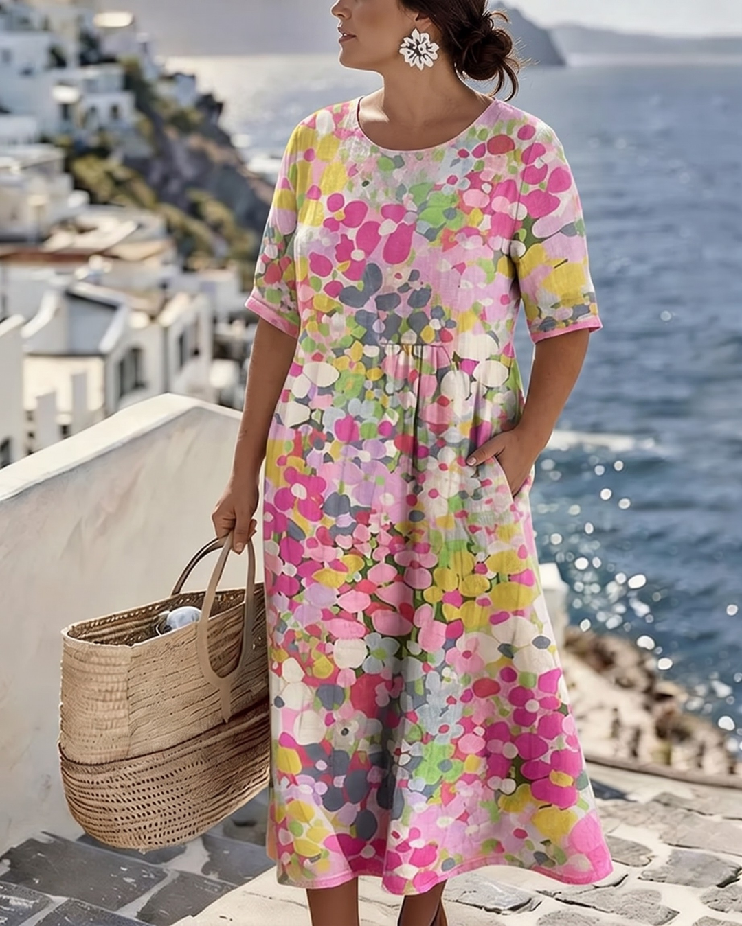 Model wearing vibrant floral midi dress by the sea, holding wicker bag, with scenic coastal view.
