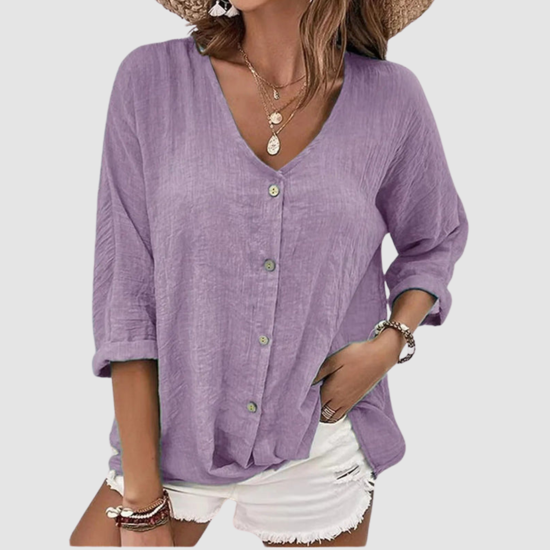 Woman wearing a purple V-neck blouse with buttons, accessorized with necklaces and bracelets, paired with white shorts against a plain background.
