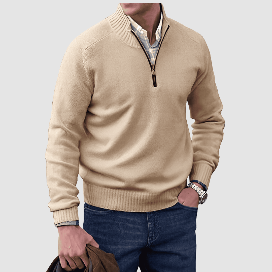 Model in beige zip pullover with ribbed collar and cuffs, holding a jacket. Paired with jeans, set against a plain background.