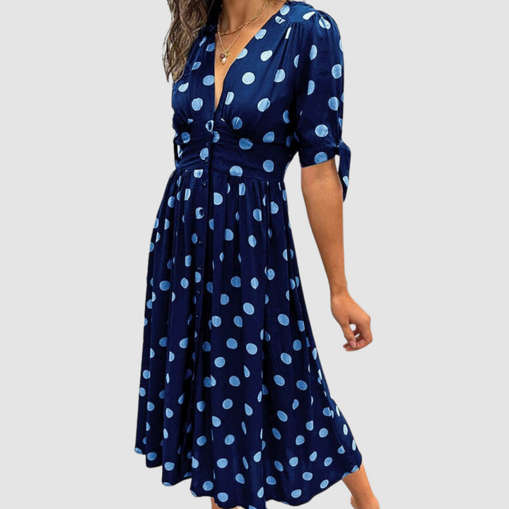 Navy dress with light blue polka dots, V-neck, tied sleeves, knee-length, studio setting.