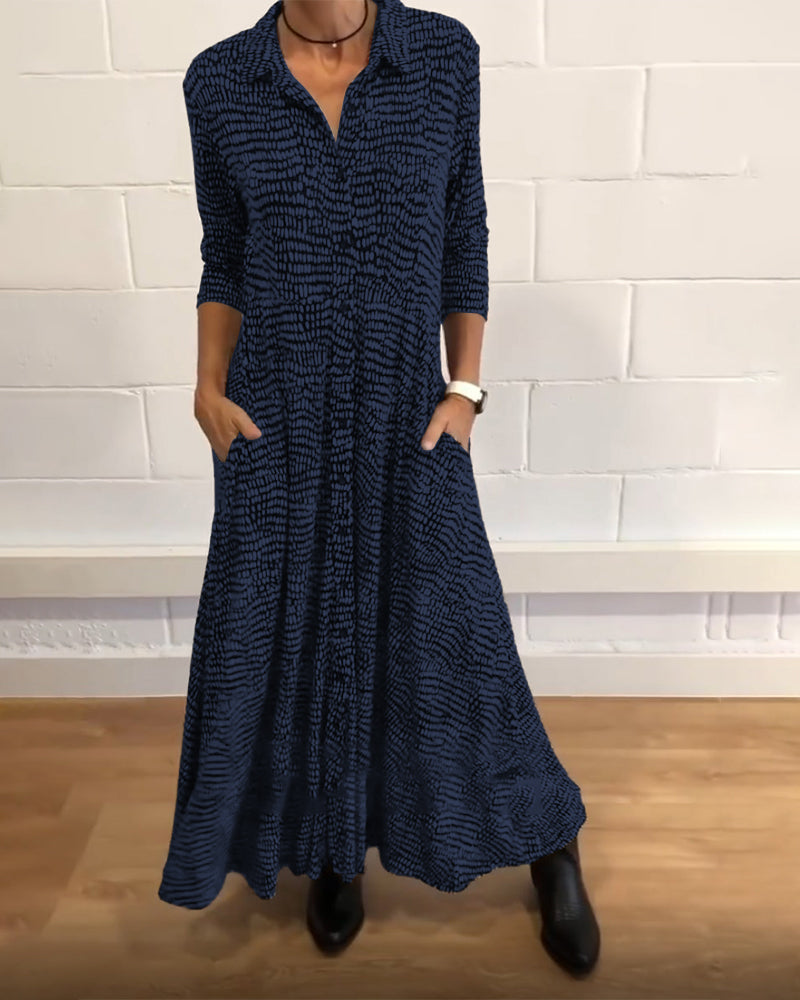 Navy-patterned maxi dress with 3/4 sleeves and collar, worn indoors against a white brick wall.