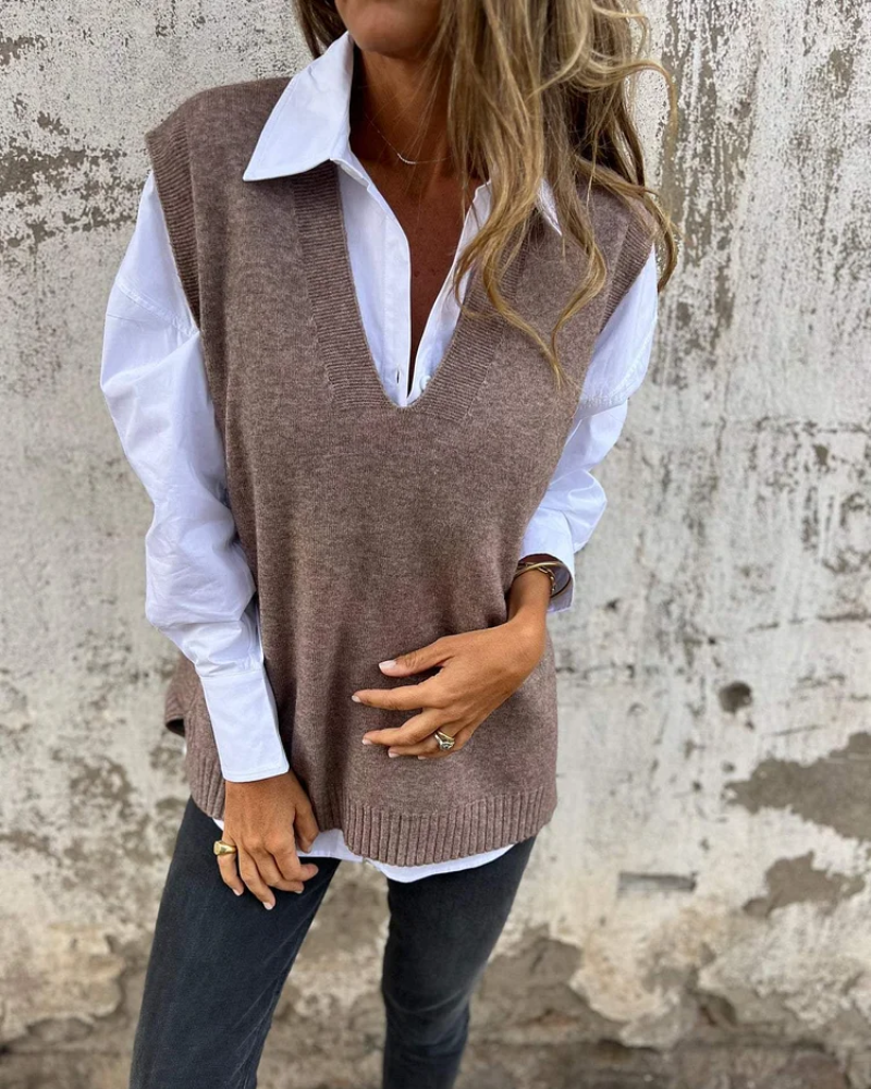 Brown knit vest layered on a white shirt, styled by a person against a rough wall backdrop.