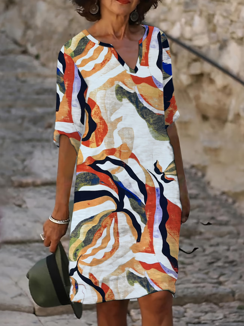 Woman wearing a vibrant, abstract-patterned summer dress with red, orange, and blue swirls, standing on stone stairs.