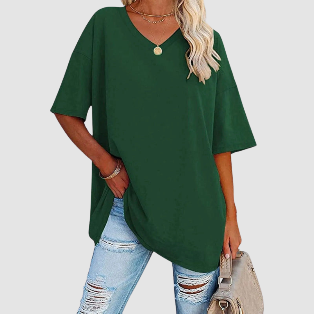 Woman in a green V-neck T-shirt with distressed jeans, carrying a beige bag, studio setting.
