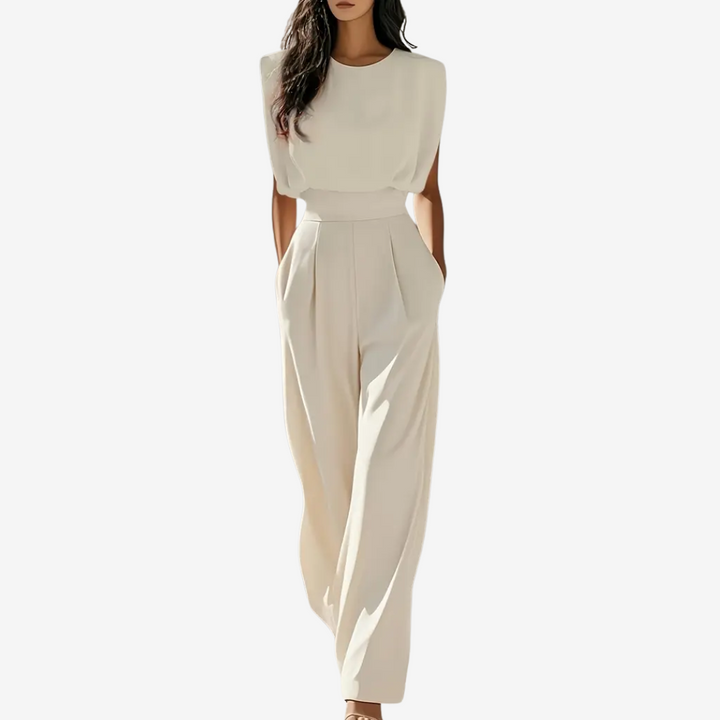 Cream sleeveless jumpsuit with wide legs, worn by model in studio setting, hands in pockets.