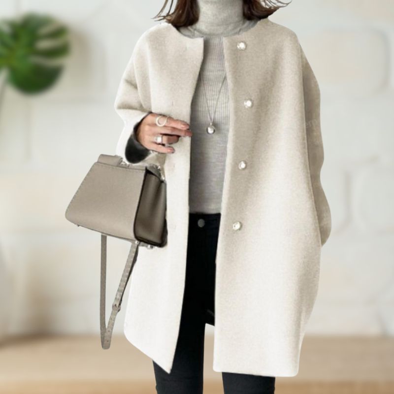 Cream mid-length coat paired with a light turtleneck and black pants, complemented by a beige handbag in a chic indoor setting.