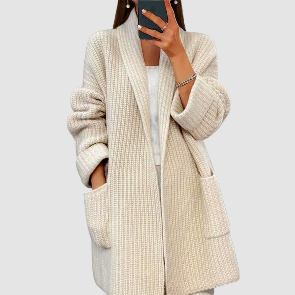 Close-up of a white knitted cardigan worn by a person taking a mirror selfie against a neutral background.