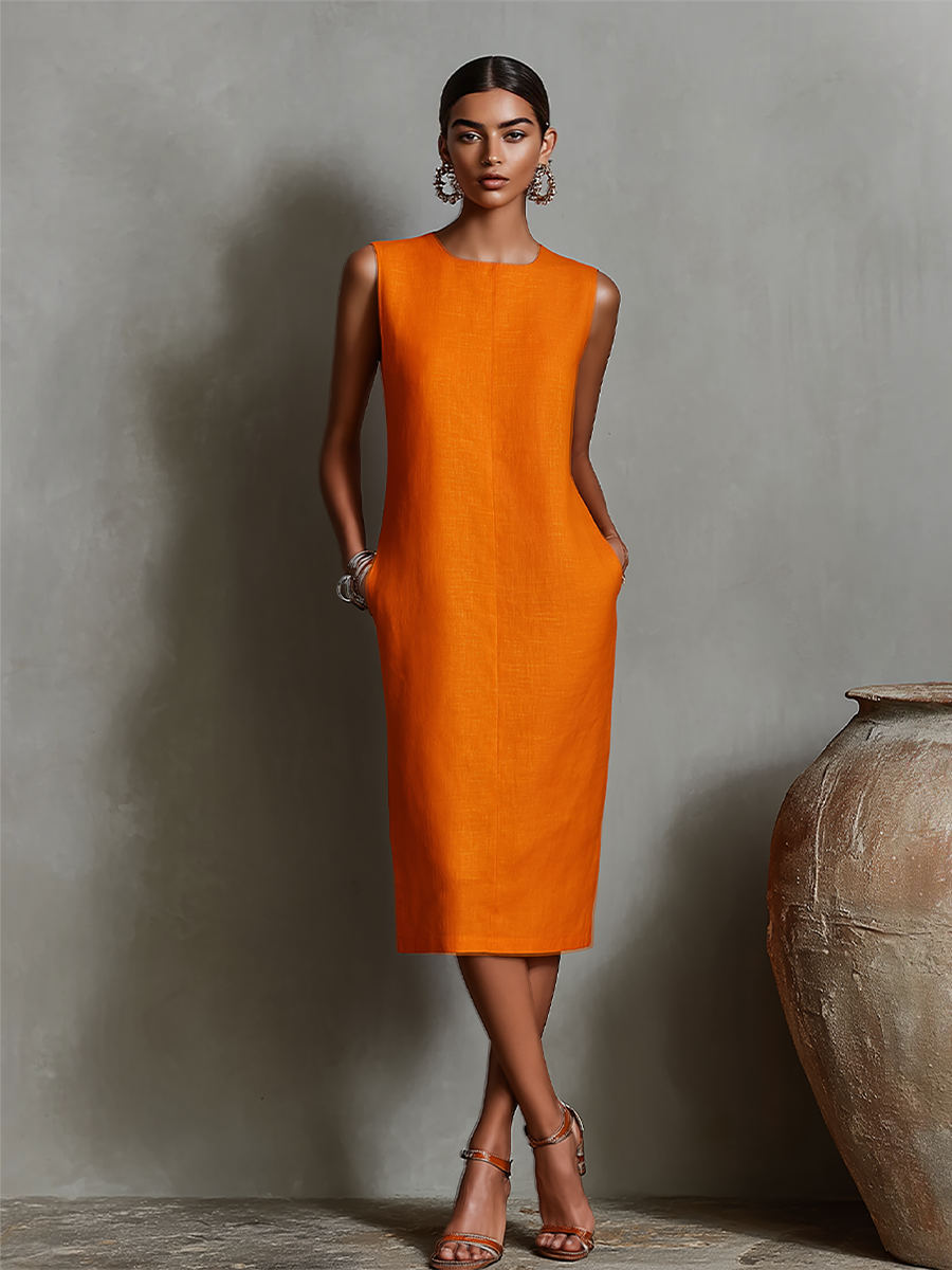 Model wearing orange midi dress with pockets, sleeveless, against a textured gray wall in studio.