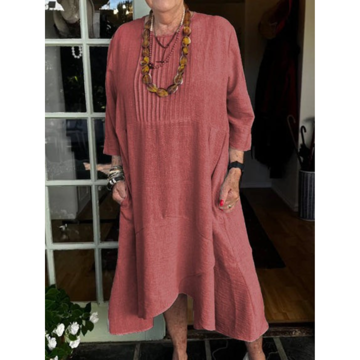 Woman in a red pleated dress with irregular hem, accessorized with necklaces in a boutique setting.