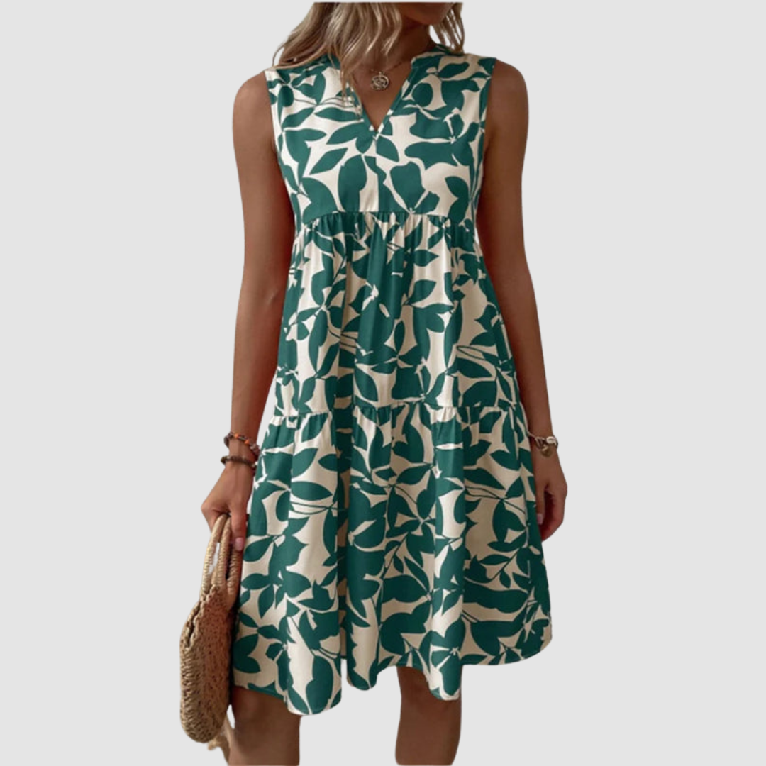 Model wearing a sleeveless green and white floral print flowy dress, holding a woven bag, against a plain background.