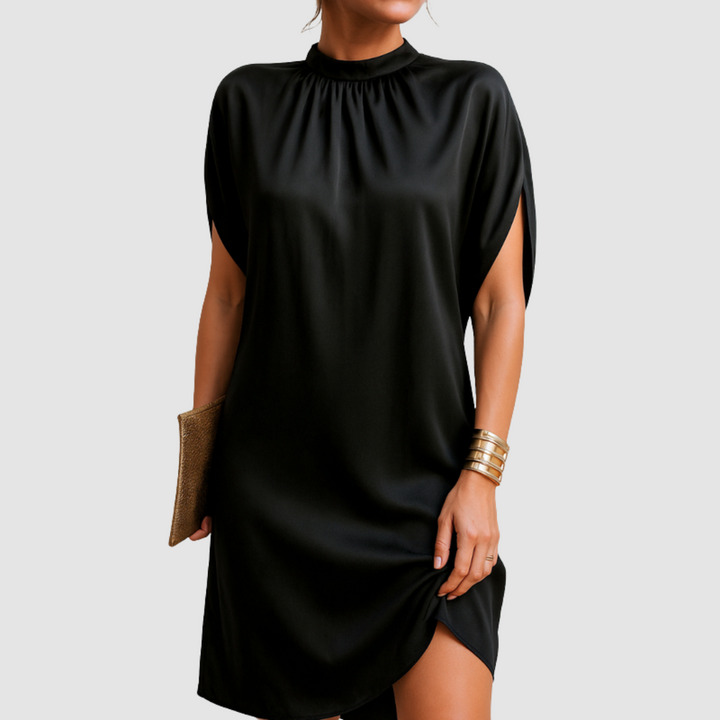 Black knee-length dress with loose, elegant fit and high neckline, modeled with gold bangles and clutch against gray background.