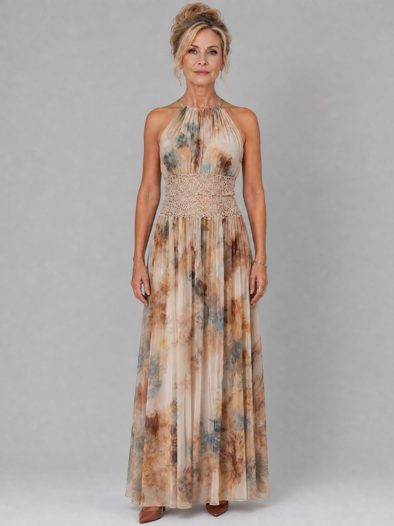 Elegant woman in a halter neck maxi dress with lace waist, earthy tones, standing in front of a plain grey backdrop.