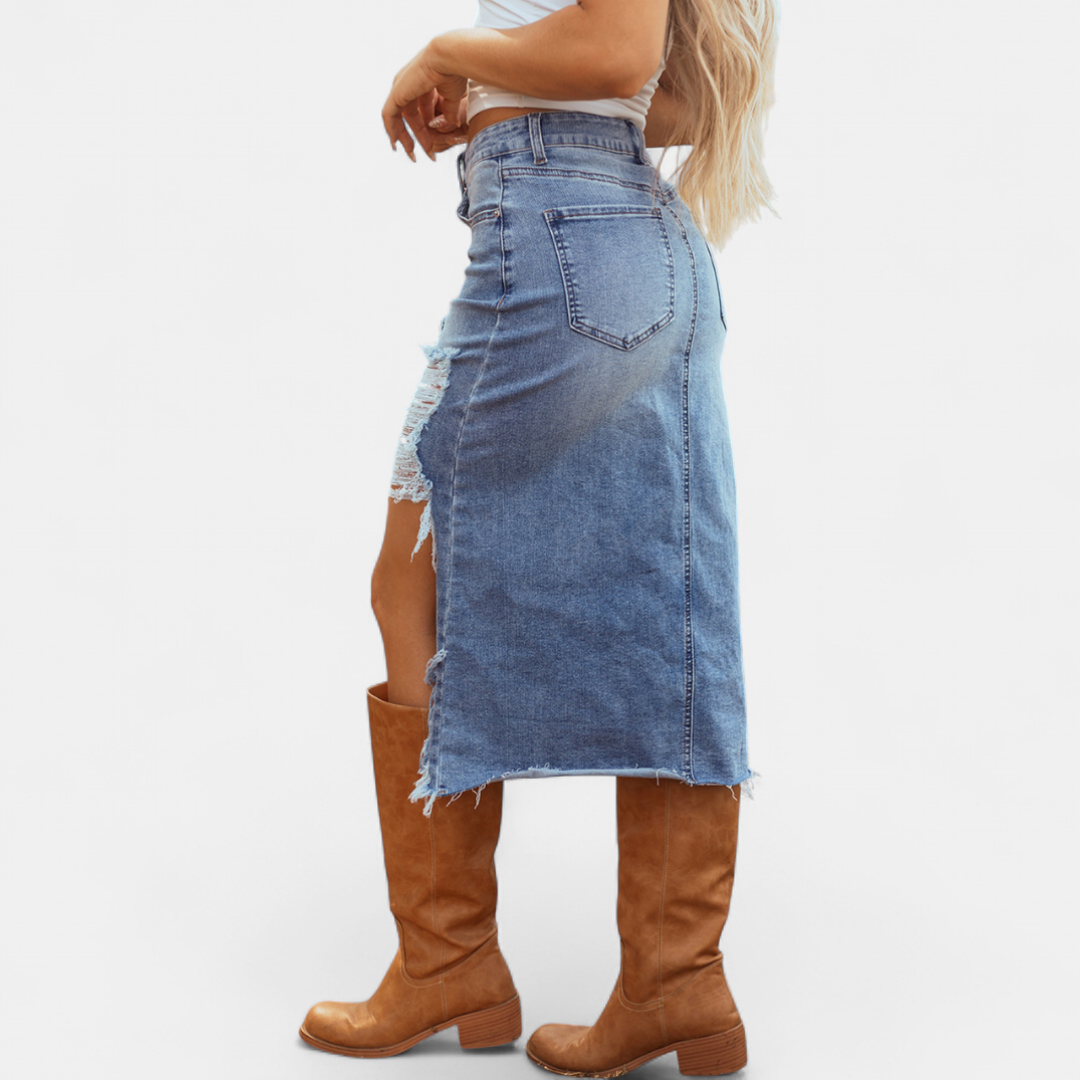 Side view of a distressed high-waist denim maxi skirt with a white top and brown boots in a studio setting.