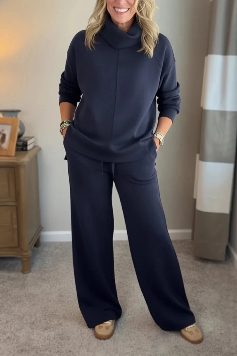 Woman in a navy comfortable set with long sleeves and wide-leg pants, standing in a carpeted room with a wooden table nearby.