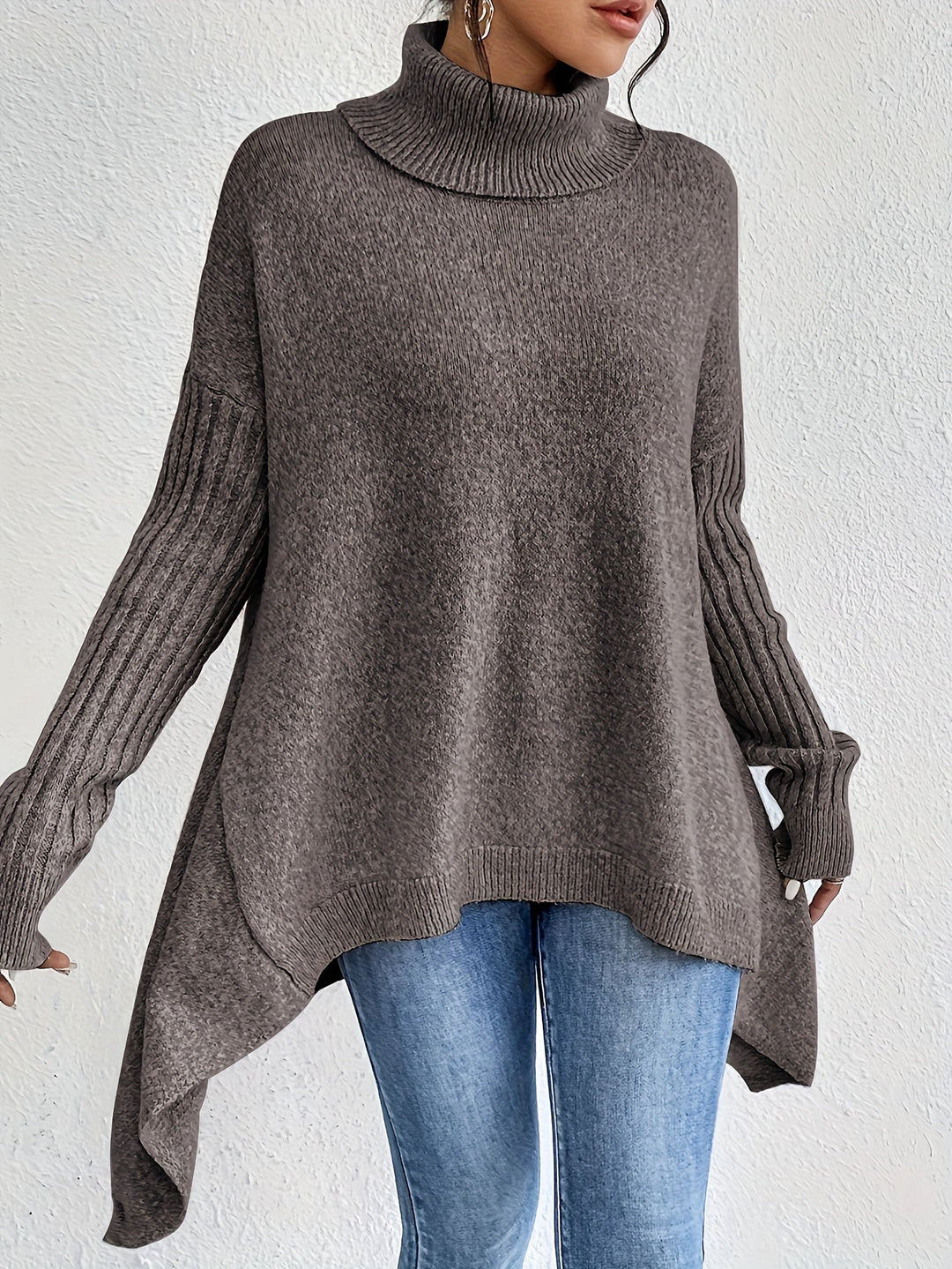 Brown turtleneck sweater with ribbed sleeves, worn with jeans, positioned against a plain white wall.